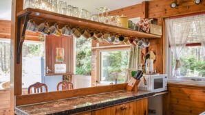 A kitchen with wooden cabinets, a granite countertop, a microwave, and a variety of mugs hanging above the counter.