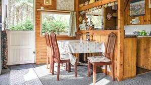 A wooden cabin interior with a dining area, a kitchen with a wooden counter, and a large window offering a view of the forest.
