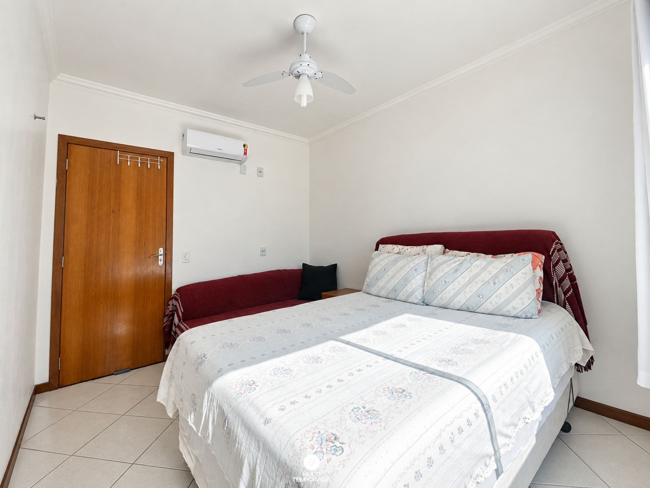 Un dormitorio con una cama, un ventilador de techo, un equipo de aire acondicionado y una puerta de madera.