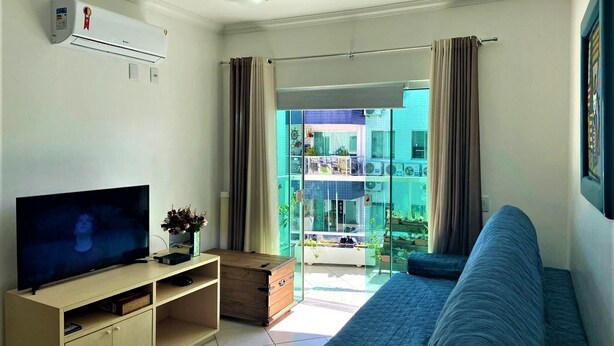Uma sala de estar com televisão de tela plana, móvel de entretenimento de madeira, sofá azul e ventilador de teto.