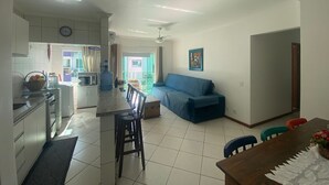 Uma cozinha moderna com armários brancos, uma área de jantar com mesa de madeira e um sofá azul na sala de estar.