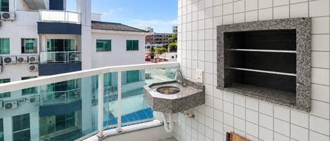 Un balcón moderno con barandilla de vidrio, un lavamanos integrado y vistas a la ciudad.