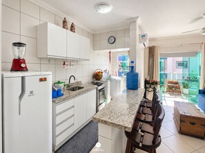 A modern kitchen with white cabinets, a granite countertop, a red blender, and a large blue water dispenser.
