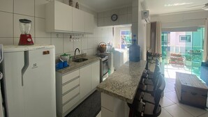 Cozinha com armários brancos, bancada de granito, lava-louças embutida, liquidificador, pia e um grande dispensador de água.