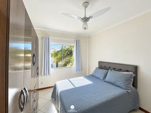 Une chambre à coucher avec un lit, un ventilateur de plafond, une fenêtre avec des rideaux et une armoire.
