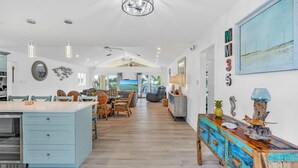 A spacious kitchen with a central island, a dining area with wicker chairs, and a large window overlooking the beach. - Private Pool, Hot Tub, Boat Dock, Putting Green (Marathon)