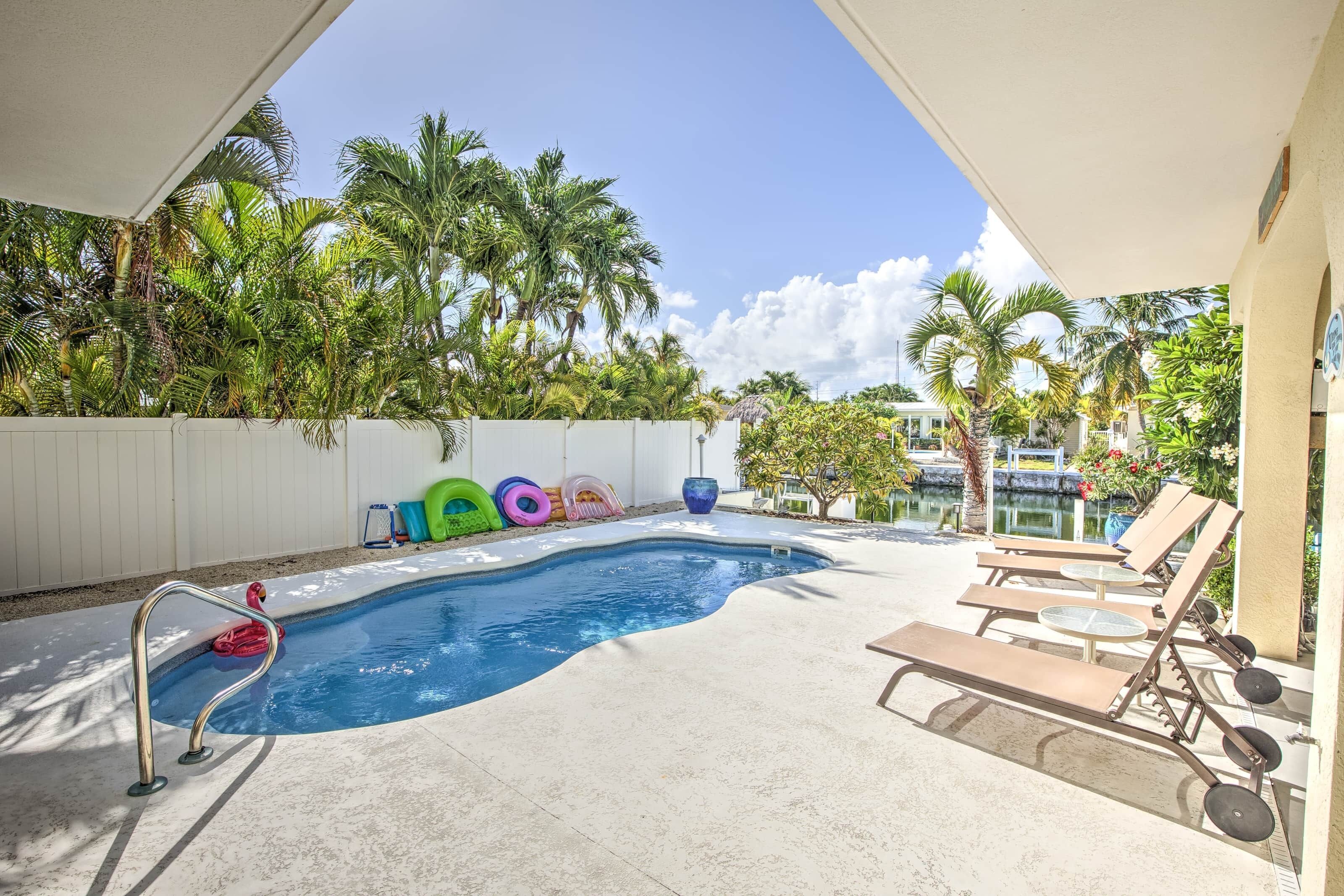 A swimming pool with lounge chairs and colorful inflatable rings.