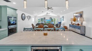 A spacious kitchen with a central island, dining area with wicker chairs, and a large window offering a view of the outdoors. - Private Pool, Hot Tub, Boat Dock, Putting Green (Marathon)