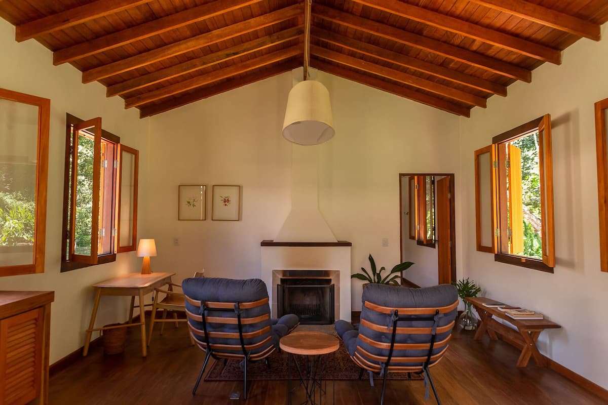 Un salon chaleureux avec une cheminée, des poutres apparentes en bois et de grandes fenêtres.