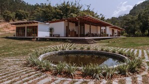 A modern house with a covered patio, a small pond, and a garden with tropical plants. - Fazenda Santa Vitória (Queluz)