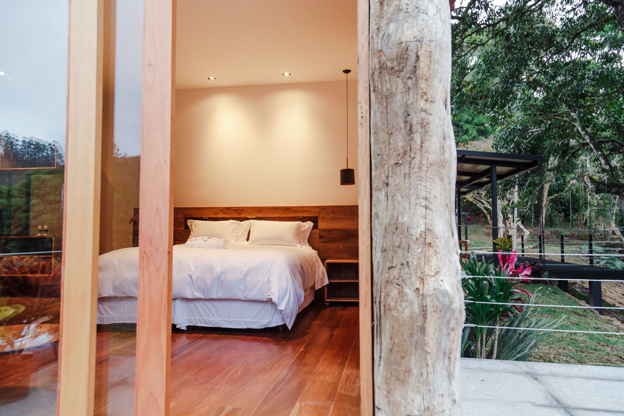 Un dormitorio con cabecera de madera, una cama grande con ropa blanca y vistas a un jardín a través de un ventanal.