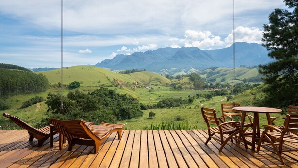 A wooden deck with a table and chairs overlooking a mountainous landscape. - Fazenda Santa Vitória (Queluz)