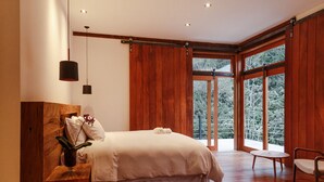 A modern bedroom with a large bed, wooden walls, and a view of trees through large windows. - Fazenda Santa Vitória (Queluz)