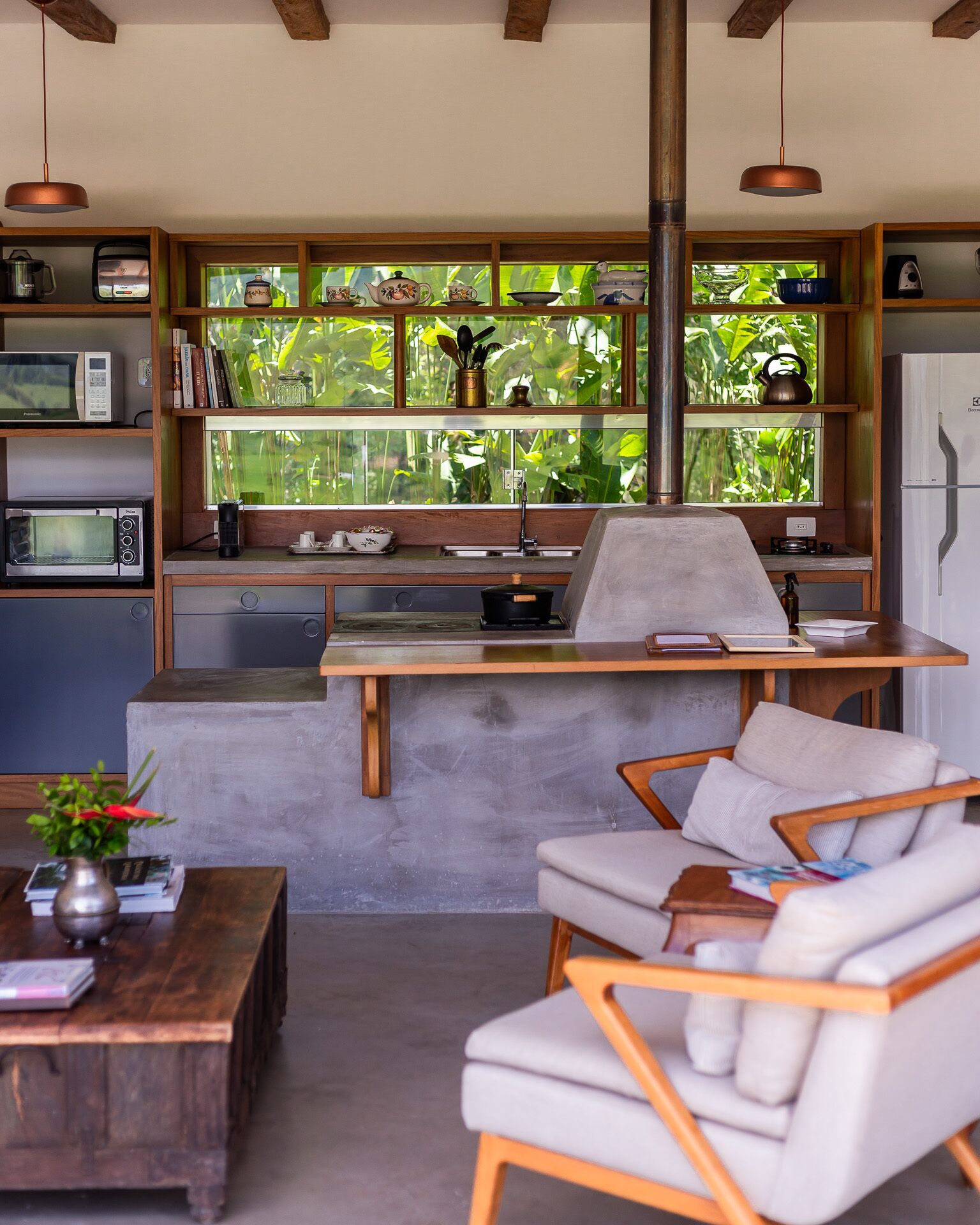 A compact kitchen with a built-in stove, microwave, and sink, wooden cabinets, and a window with a view of greenery.