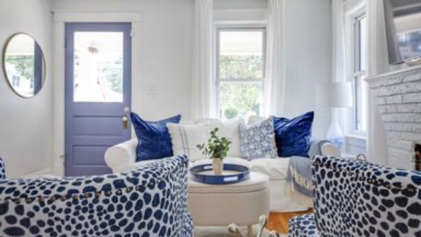 Un salon avec un canapé blanc, des fauteuils à motifs bleus, une table basse et une cheminée.
