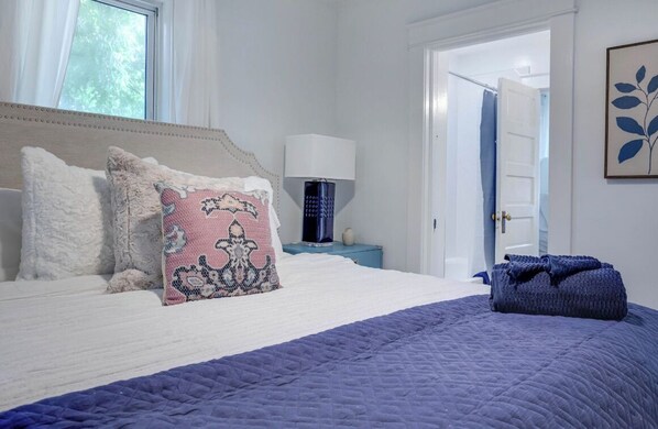 A bedroom with a bed, pillows, a nightstand, a lamp, and a door.