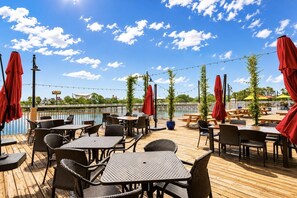 An outdoor deck with tables and chairs, red umbrellas, and a view of a body of water.