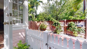 Une maison en bois avec une clôture blanche à piquets, une boîte aux lettres et un jardin où poussent différentes plantes.