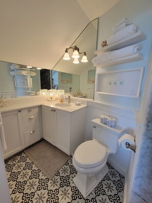 Un baño moderno con un espejo grande, accesorios blancos y baldosas de suelo estampadas.