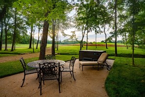 An outdoor patio with a round table and chairs, a grill, and a view of a green field and trees. - This Gives a “Cabin” a Whole New Meaning! (Carbondale)