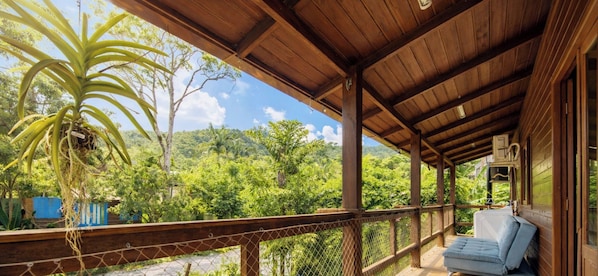 A wooden balcony with a view of lush greenery and a clear sky.