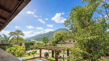 Vista de um jardim exuberante com pérgola de madeira, piscina e montanha ao fundo.