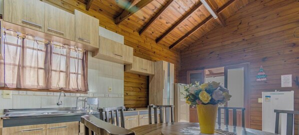 A wooden interior with a kitchen, dining area, and a window with curtains. - Casa com Piscina em Gov Celso Ramos - SC (Governador Celso Ramos)