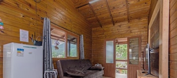 Interior de una cabaña de madera con sofá, refrigerador y televisión.