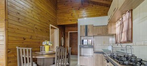 A wooden interior with a kitchen area, including a dining table with chairs, a small round table with a vase, and a stove. - Casa com Piscina em Gov Celso Ramos - SC (Governador Celso Ramos)