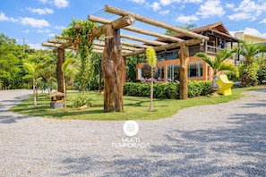 A wooden pergola structure with climbing plants, a well-maintained lawn, and a building with a tiled roof in the background.