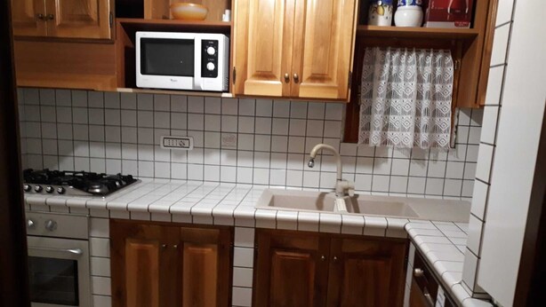 A kitchen with wooden cabinets, a microwave, a stove, and a sink. - Apartment on the 2nd Floor 5 min from the spa (Saint-Vincent)
