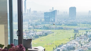 A modern hotel room with a large window offering a city view, a marble table, and a vase of flowers. - Most Luxurious Property in Puebla - Ultra Luxurious 4 Bedrooms 4.5 Bath - Pool (Tx)