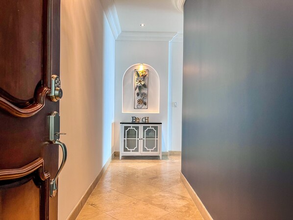 Un pasillo con una puerta de madera, un armario blanco con puertas de cristal y una obra de arte colgada en la pared.
