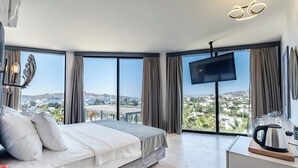 A modern hotel room with a large bed, a flat-screen TV, and a view of a cityscape through large windows. - Bombien Yalıkavak (Bodrum)