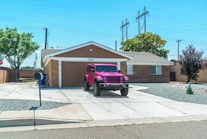 Ein pinkfarbener Jeep steht auf einer Auffahrt vor einem Haus mit Garage, Hausnummer 7608.