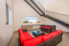 A spacious living area with a staircase, a large window with a view, and a seating area with red cushions.