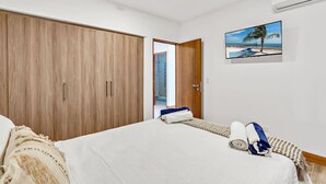 Ein Schlafzimmer mit einem Bett, einem Holzschrank, einem an der Wand montierten Fernseher und einer Tür zu einem anderen Raum.