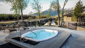 Un bain à remous sur une terrasse en bois, agrémentée de chaises longues, entouré d’arbres et offrant une vue sur la montagne.