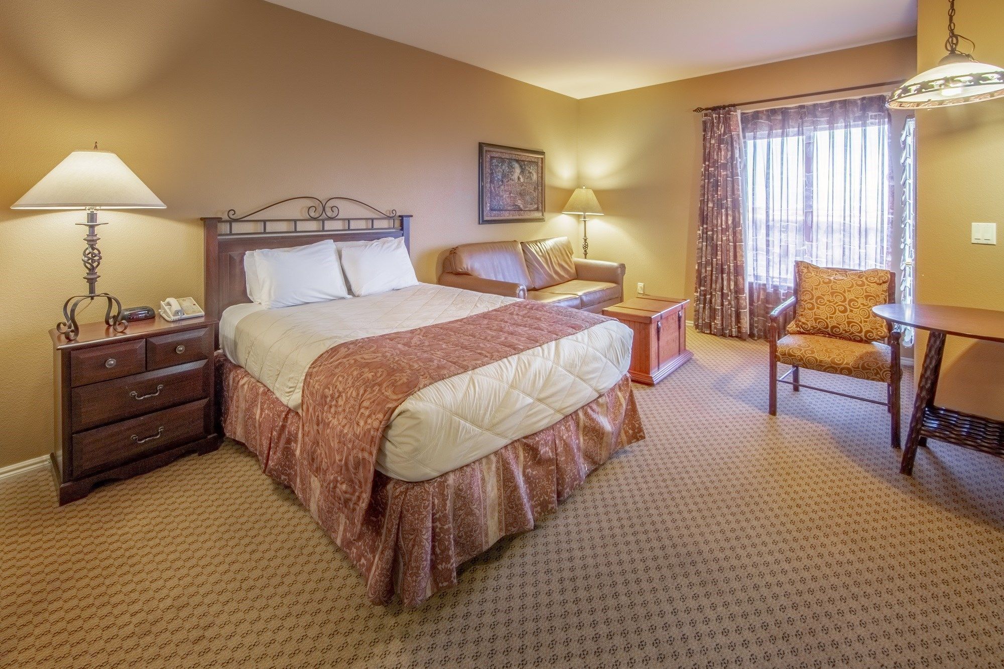 A hotel room with a bed, a desk, a chair, a nightstand, and a lamp.