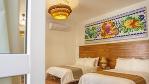 Habitación de hotel con dos camas, piso de madera, candelabro, unidad de aire acondicionado y un mural colorido en la pared.