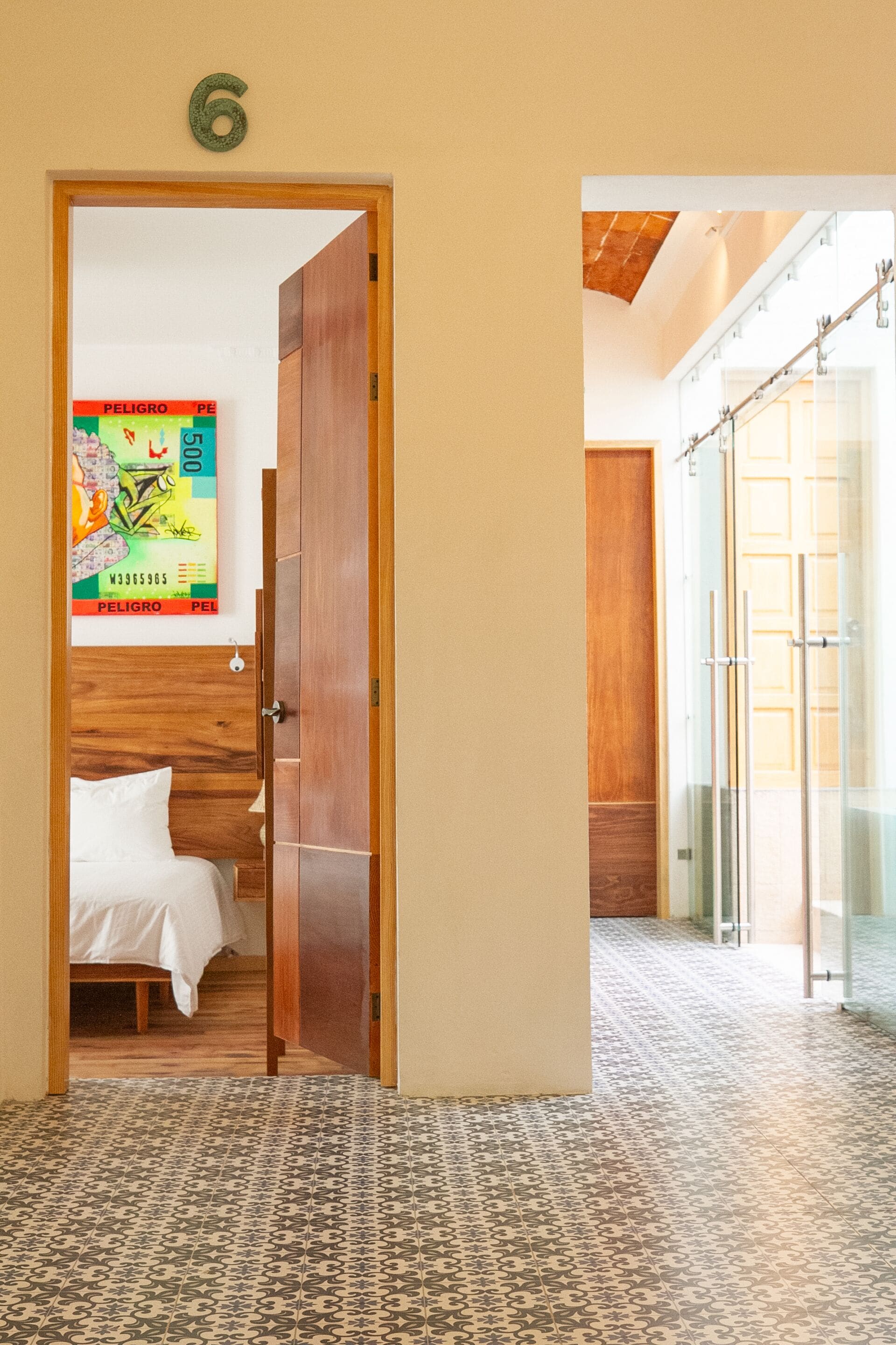 A hotel room with a bed, a wooden door, a tiled floor, and a glass shower area.