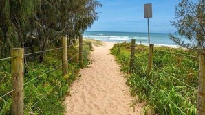 A sandy beach path with a wooden fence and a signpost, leading to the ocean. - Unit 4 Sundeck Gardens (Sunshine Coast)