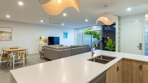 A modern kitchen with a white countertop, wooden cabinets, and a built-in dishwasher. - Unit 4 Sundeck Gardens (Sunshine Coast)