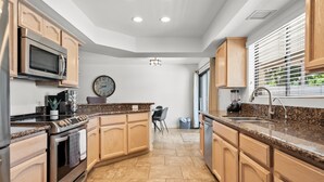Eine moderne Küche mit Granit Arbeitsplatten, Edelstahlgeräten, Holzschränken und einer eingebauten Mikrowelle.