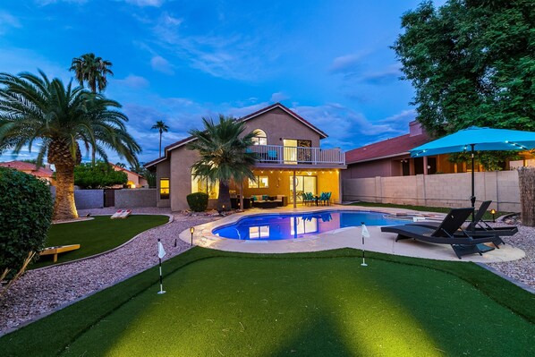 A house with a swimming pool, a balcony, and a well-maintained lawn.