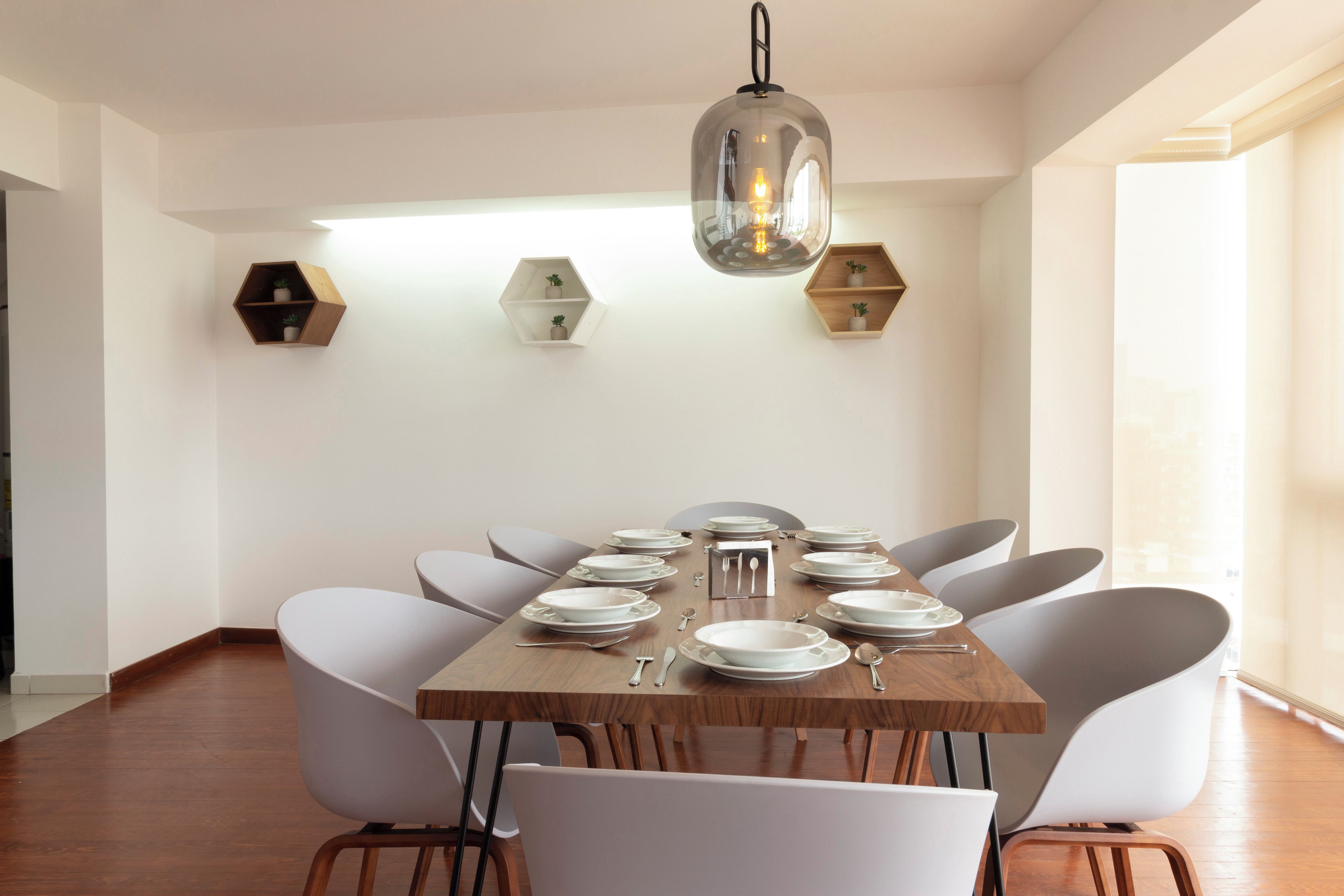 Comedor con una mesa de madera dispuesta para seis personas, rodeada de sillas blancas, con una lámpara colgante.