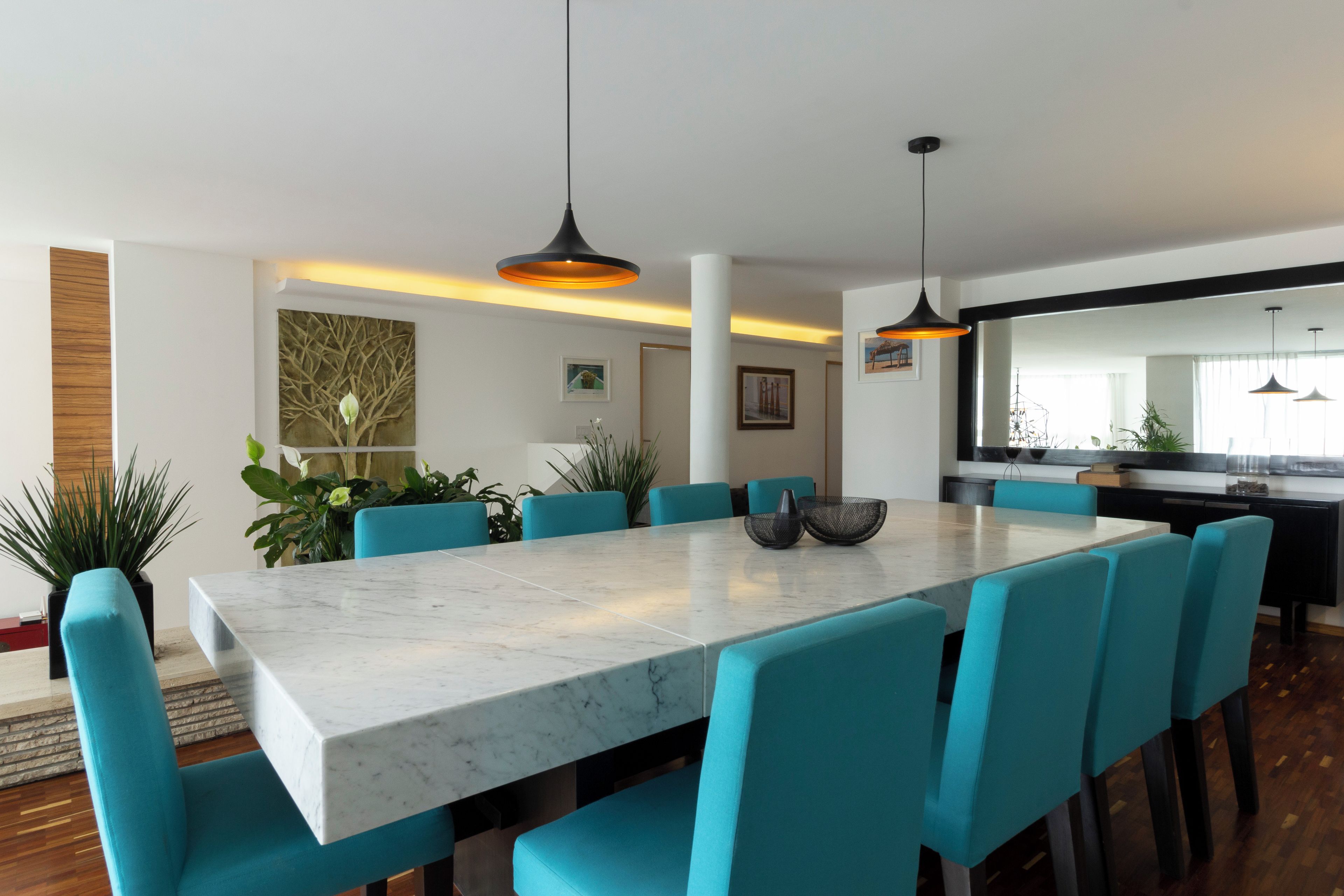 Un comedor moderno con una mesa de mármol, sillas color aguamarina e iluminación colgante.