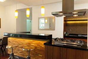 A modern kitchen with a black countertop, wooden accents, a gas stove, and pendant lighting.