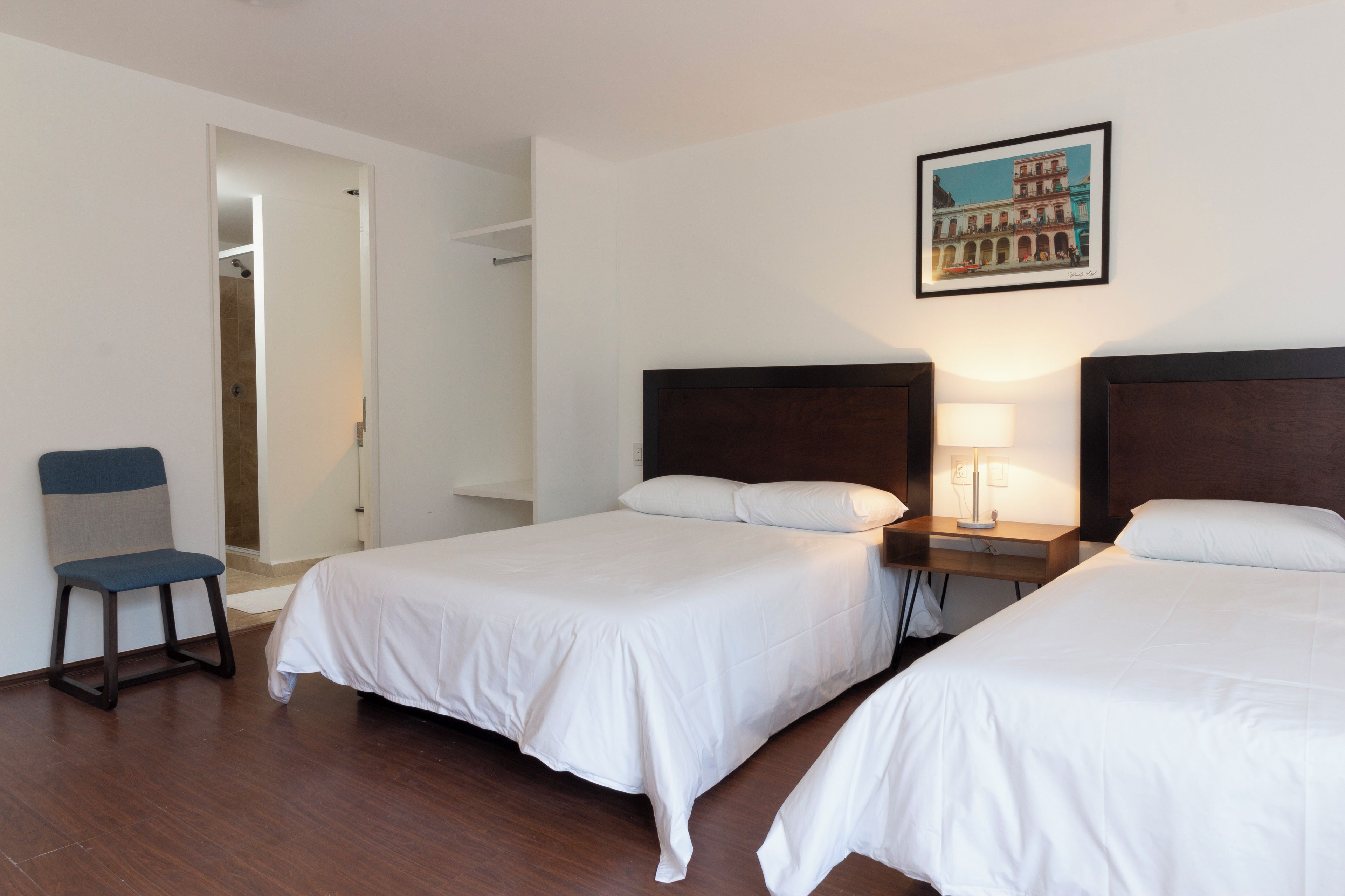 A hotel room with two beds, a chair, a nightstand, and a painting on the wall.
