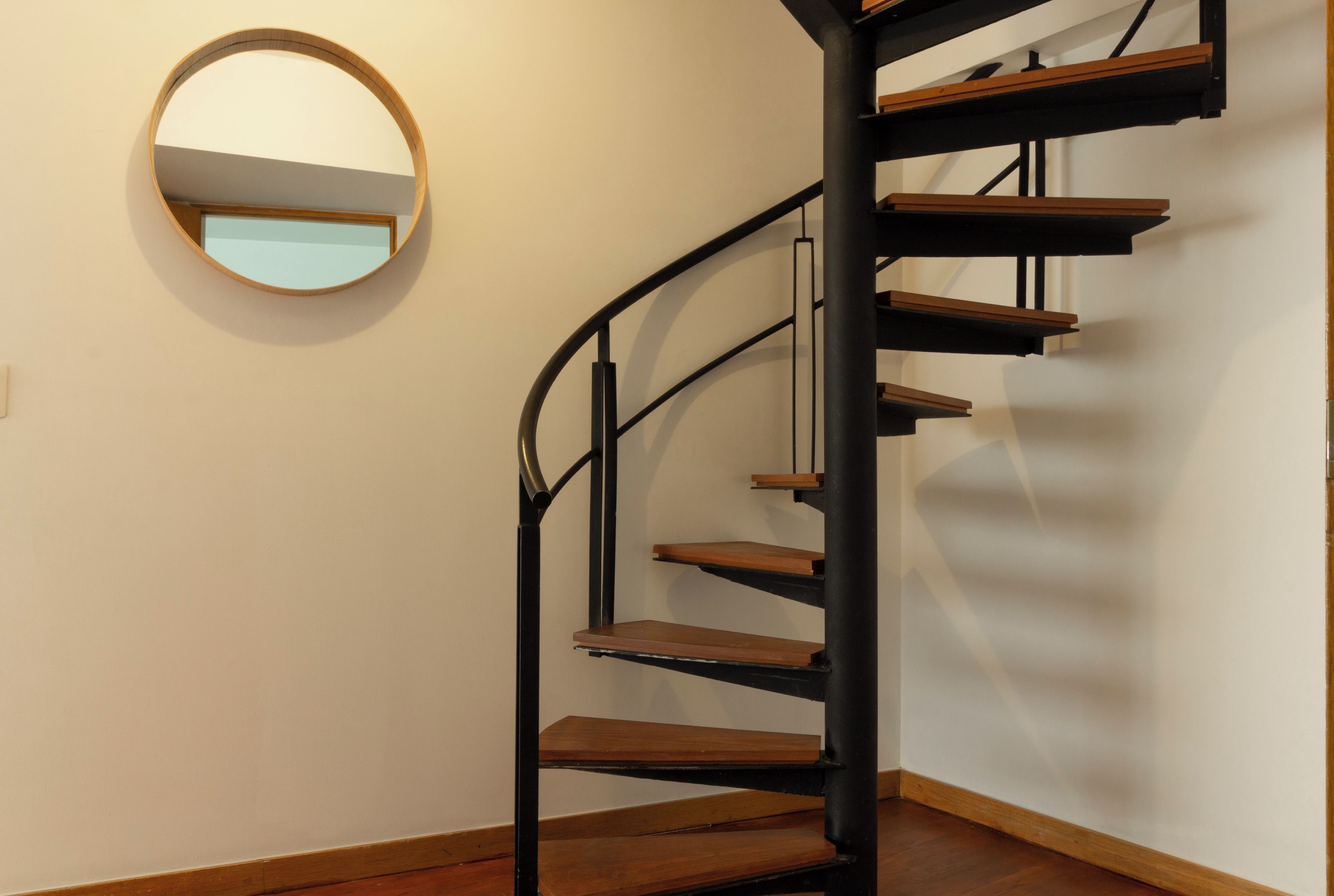 Una escalera de caracol con escalones de madera y barandillas de metal negro, que sube a un piso superior.